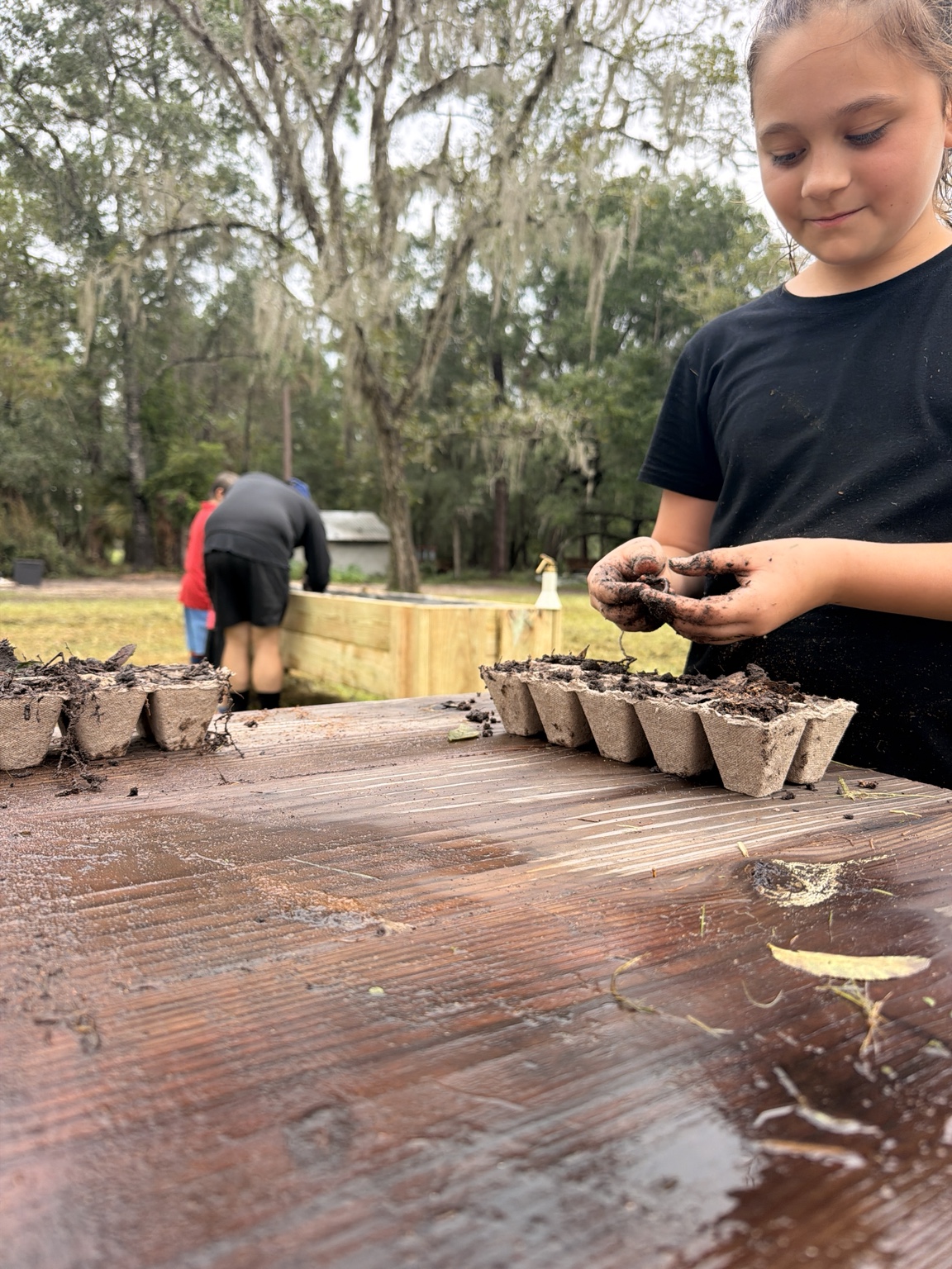 An ORVIT student planting seeds with muddy hands at the outdoor garden table