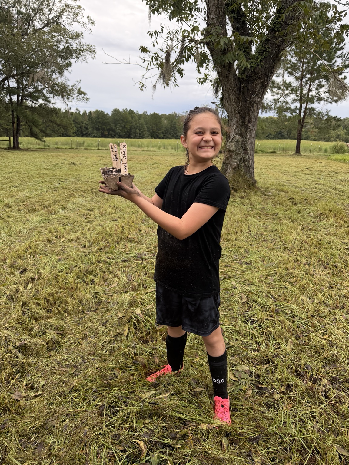 A smiling ORVIT student holding a tray of newly planted seeds outdoors